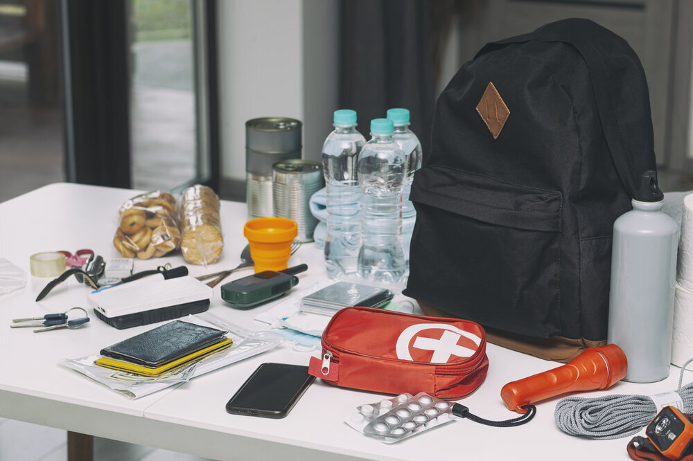 Rucksack-Notfallausrüstung auf dem Tisch. Dokumente, Wasser, Lebensmittel, Verbandskasten und andere Dinge, die zum Überleben benötigt werden.