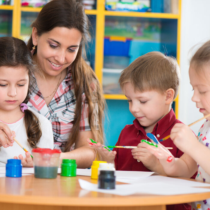 Frau sitzt am Tisch mit 3 Kindern und malt